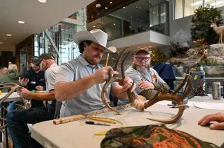 Two men measure antlers from a harvested deer. 