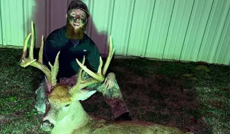 Colton Mayberry is posing with a large grin behind his harvested whitetail buck.