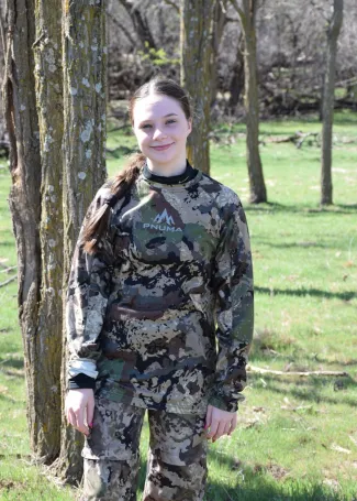 a young girl in the woods wearing camo about to hunt