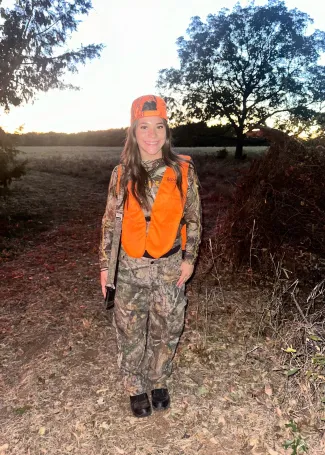 a young girl in the woods wearing camo and hunters orange about to hunt