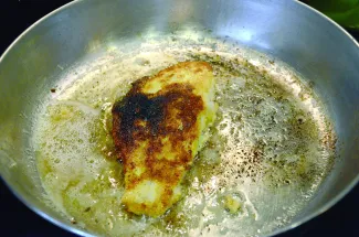 A breaded fish filet is being fried in a pan.