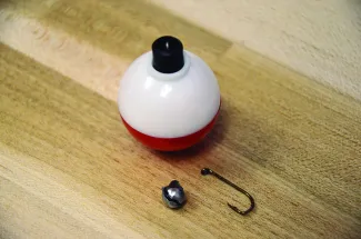 A hook, weight and bobber are displayed on a wooden background.