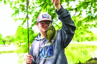 An Oklahoma student shows off his catch, holding the fish on the line in front of him.