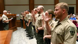 Game Wardens are pledging their oath at their badge pinning ceremony. They are lined up with their right hands lifted as they repeat their oath.
