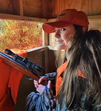 young lady sitting in deer blind holding rifle