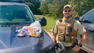Oklahoma Game Warden Gillham stands next to evidence of snake skins piled on his  truck's hood.